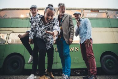 Les 4 artistes du groupe Oliv' et ses noyaux devant un vieux bus impérial vert