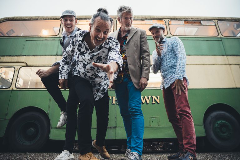 Les 4 artistes du groupe Oliv' et ses noyaux devant un vieux bus impérial vert