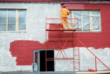 Peintre sur un échafaudage en train de peindre une façade en rouge