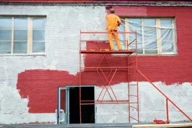 Peintre sur un échafaudage en train de peindre une façade en rouge