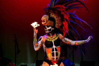 Danseur grimé avec coiffe et peinture corporelle, tenant du feu au bout de ses doigts