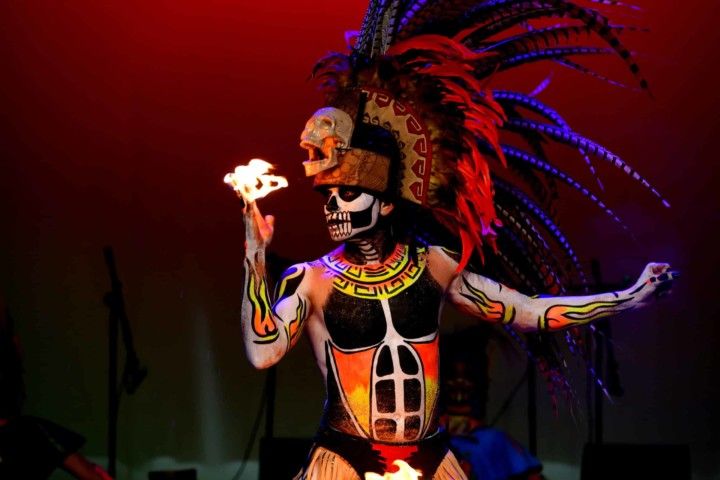 Danseur grimé avec coiffe et peinture corporelle, tenant du feu au bout de ses doigts
