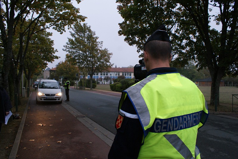 Gendarme avec un gilet fluo jaune en train de réaliser un contrôle de vitesse sur la rue des écoles