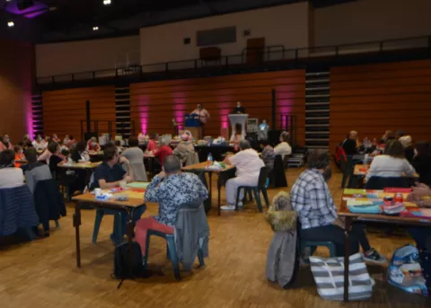 Photo du loto octobre rose de 2020. Des tables avec des joueurs et une scène au fond, des spots roses