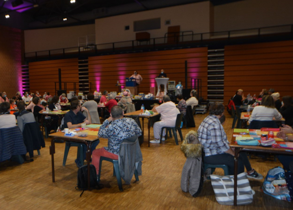 Photo du loto octobre rose de 2020. Des tables avec des joueurs et une scène au fond, des spots roses