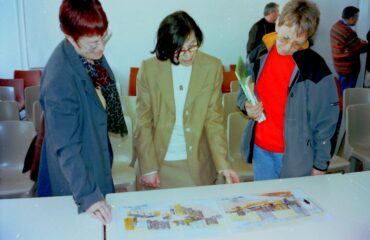 Photo des années 2000 où trois personnes consultent les plans de la future bibliothèque présentée lors d'une réunion publique.