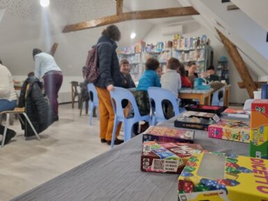 au premier plan jeu de société sur une table à l'arrière plan des familles en train de jouer autour d'une table.