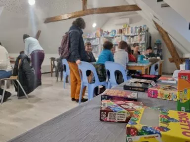 au premier plan jeu de société sur une table à l'arrière plan des familles en train de jouer autour d'une table.