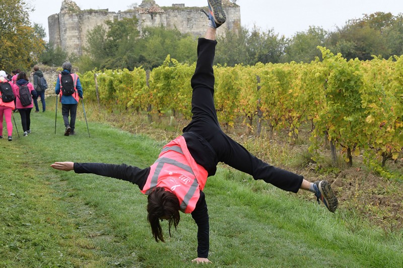 Jeune fille avec un gilet rose en appui sur une main avec en arrière plan les vignes et le château de Montfaucon
