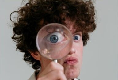 jeune homme frisée regardant à travers une loupe qui grossit exagérément son œil.