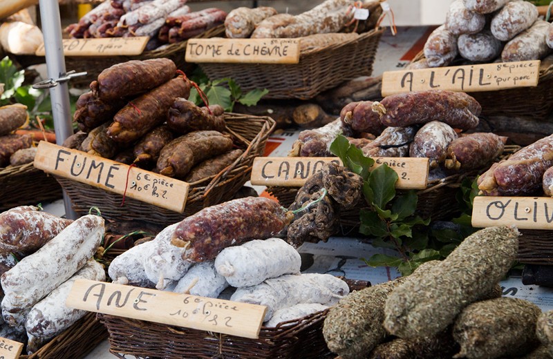 présentation de différentes sortes de saucissons secs sur un étal de marché.