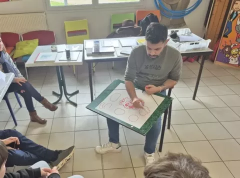 Sylvain Molossy, planche de dessin sur les genoux, explique aux jeunes comment à partir d'un dessin en forme de patate on peut créer un personnage.