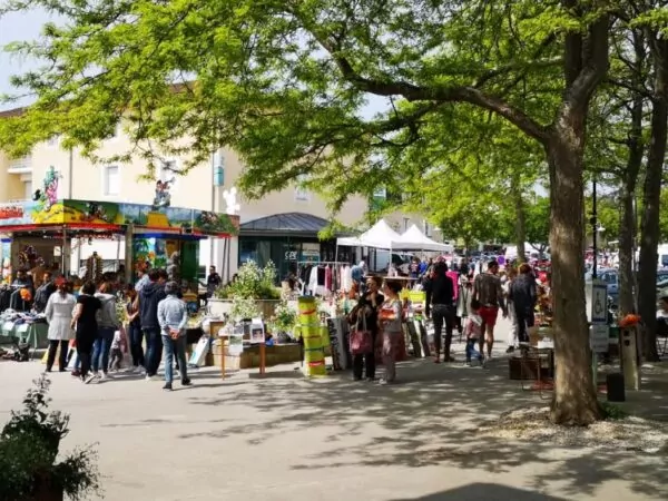 Vide grenier du Comité des fêtes de Jaunay sur la place de la fontaine. Des stands, des visiteurs et une manège en second plan