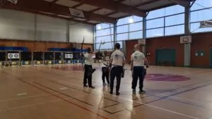 Groupe de 3 archers dans le gymnase de la Haute Payre devant les cibles prêts à tirer.