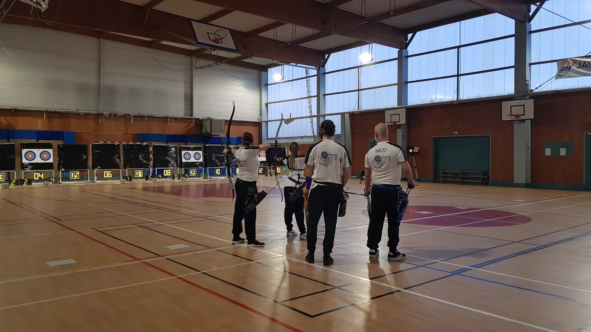 Groupe de 3 archers dans le gymnase de la Haute Payre devant les cibles prêts à tirer.