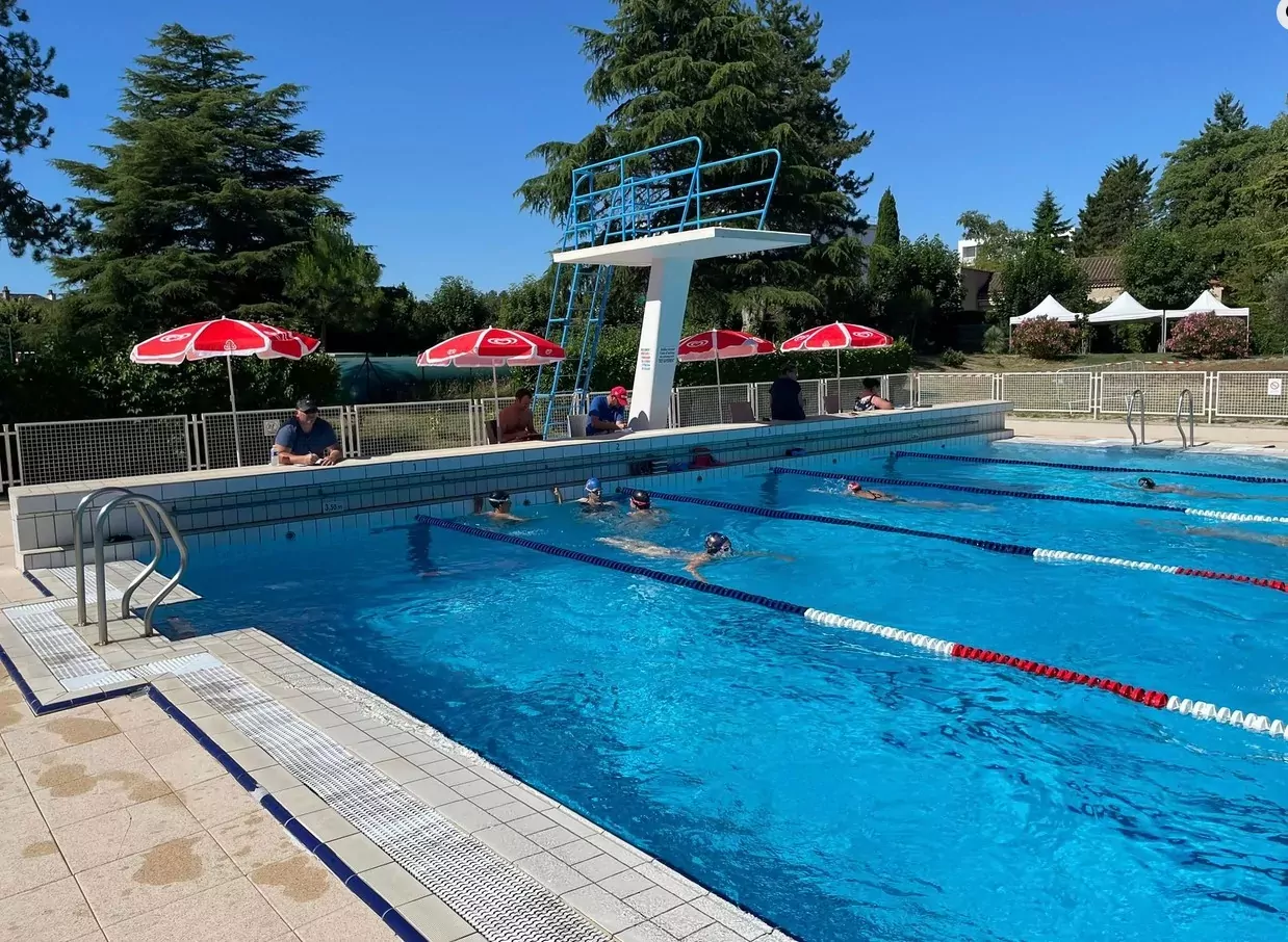 piscine de Jaunay-Marigny équipée de ses 4 lignes d'eau dans lesquelles des nageurs évoluent bonnet sur la tête. Sous les parasols en bout de piscine, des membres du club nautique comptent les longueurs.