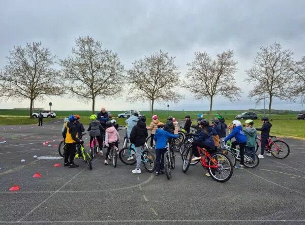 Enfant en groupe avec leur vélo sur un parking écoutant les consignes du policier municipal