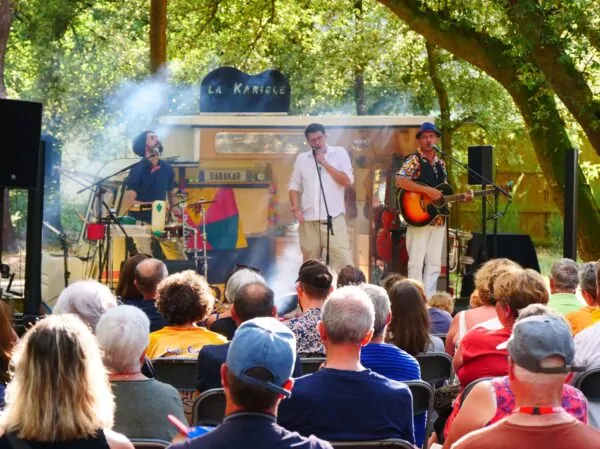 Les trois artistes du groupe Babakar sur la scène de leur Kariole devant un public assis.