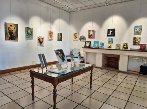 Salle d'exposition de la Maison des Arts où sont exposées les peintures de Patrick Savigny. Au premier plan une table sur laquelle il y a des peinture présentées sur des chevalets.