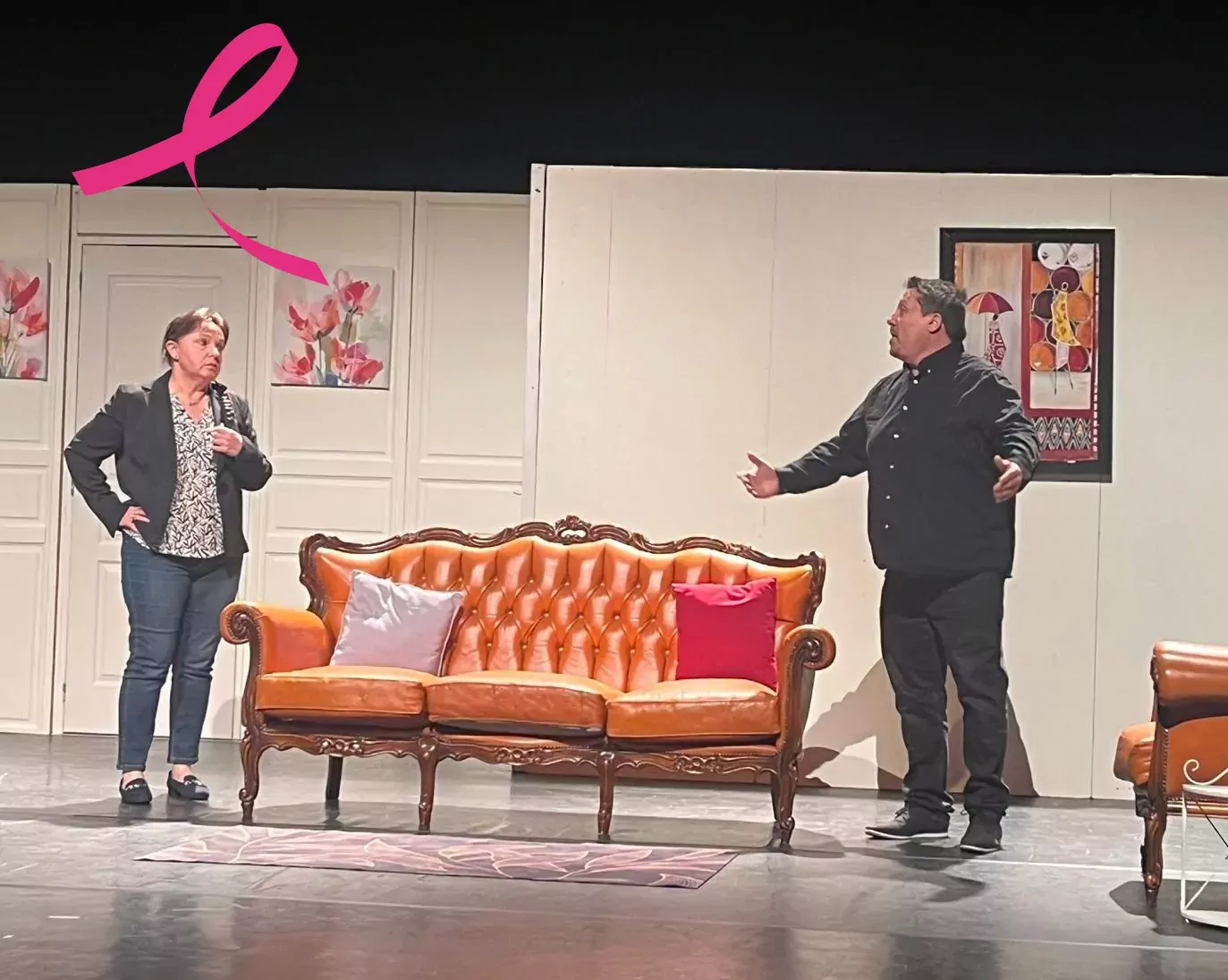 Sur un plateau de théâtre, deux acteurs debout de chaque côté d'un canapé
