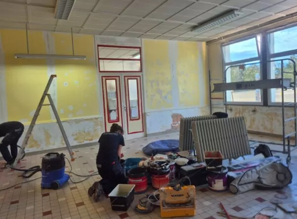 Salle de classe en travaux ou deux jeunes filles sont au milieu de leur matériel pour la peinture